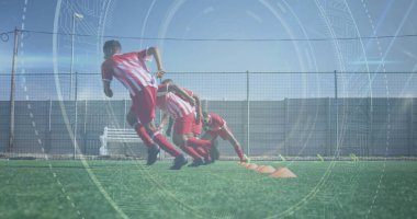 Bir grup çift ırklı sporcu futbol sahasında antrenman yapıyor. Kırmızı ve beyaz çizgili üniforma ve siyah şort giyiyorlar.