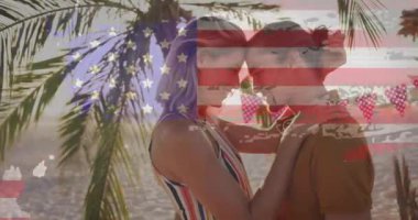 Sahilde palmiye ağaçlarının altında kucaklaşan çift üzerine Amerikan bayrağı animasyonu. Vatanseverlik, romantizm, tatil, aşk, tropik