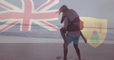 Kumsalda yürüyen, elinde İngiliz bayrağı, Turks ve Caicos arması olan bir çift. Seyahat, vatanseverlik, tatil, tropik, sahil, kutlama
