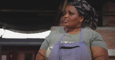 Front view of an African female butcher wearing a headscarf in a township workshop, cutting fresh meat with knife, slow motion