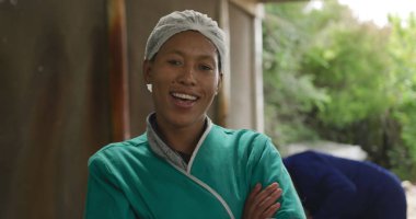 Organik bir çiftlikteki gülümseyen, melez bir kadın çiftçinin portresi, kollarını kavuşturmuş kameraya bakıyor.