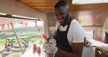 Yemek kamyonunda sosisli hazırlarken gülümseyen Afro-Amerikan bir adamın portresi. yemek kamyonu ve sokak yemekleri konsepti