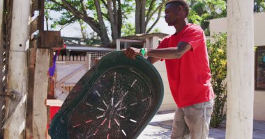 Güneşli bir günde, bir hayvan barınağında kırmızı t-shirt giyen, plastik köpek banyosu yapan Afrikalı bir gönüllü.