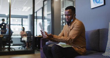Yüzü düşük Afrikalı Amerikalı adam modern ofisteki dijital tablette resim sohbeti yapıyor. Coronavirus covid 19 pan sırasında işyerinde hijyen ve sosyal mesafeler