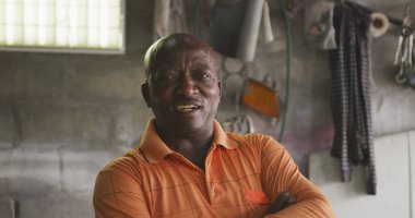 Portrait of a happy African man in a township, wearing an orange shirt and looking to camera with arms crossed, slow motion clipart