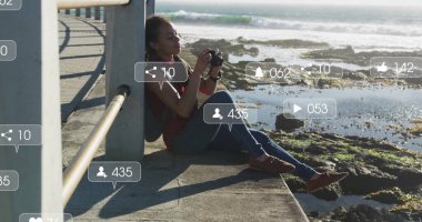 Sosyal medyada, okyanus kenarında oturup fotoğraf çeken bir kadın görülüyor. Teknoloji, fotoğrafçılık, dijital, tatil, yaşam tarzı, seyahat