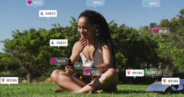 Çimlerin üzerinde oturan ve akıllı telefon kullanan, sosyal medyayla çevrili bir kadın imajı sever. Teknoloji, etkileşim, bağlılık, açık hava, dijital, bağlantı