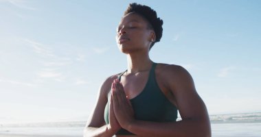 Afrika kökenli Amerikalı kadın güneşli bir günde sahilde meditasyon yapıyor. sağlıklı aktif yaşam tarzı, açık hava uygunluğu ve refahı.