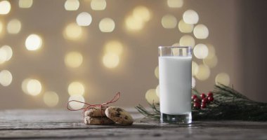 A glass of milk and cookies set on a table, evoking holiday cheer. Warm lights create a cozy, festive atmosphere, hinting at Christmas traditions. clipart