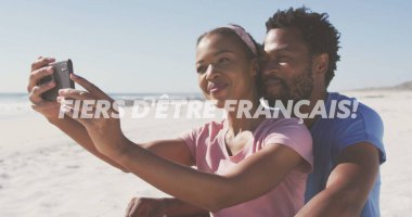 Taking selfie on beach, couple with PROUD TO BE FRENCH image. Travel, vacation, ocean, coastline, romantic, happy clipart