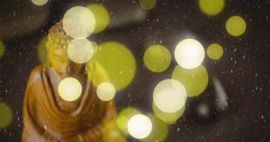 Buda heykelini çevreleyen parlak bokeh ışıkları hafif kar yağışı animasyon efektiyle. Ruhanilik, meditasyon, sükunet, sükunet, kış, aydınlanma