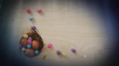 Yuvada renkli yumurtalar ve ahşap arka plan animasyonunun üzerine saçılmış şekerler. Paskalya, dekorasyon, kutlama, bahar, tatlılar, pastel