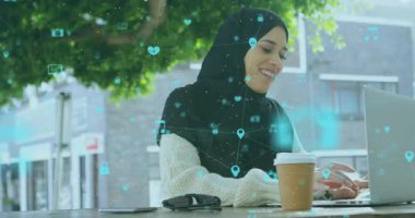 Açık havada dizüstü bilgisayar kullanan, tesettürlü kadın dijital simgelerin animasyonuyla meşgul oluyor. Teknoloji, yenilik, iletişim, bağlantı, ağ oluşturma, etkileşim
