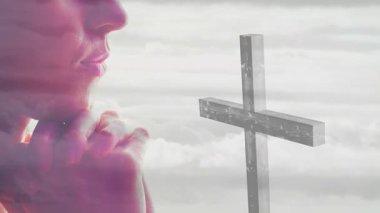 Bulutlu arka plan animasyonuyla haç tutan dua eden kişi. Maneviyat, inanç, bağlılık, din, ibadet, meditasyon