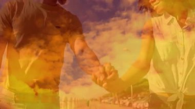 El ele tutuşan, arka planda canlı günbatımı animasyonuyla ayakta duran çift. Romantizm, bağlantı, birliktelik, siluet, ortaklık, akşam