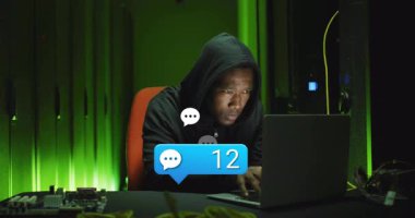 Karanlık odada dizüstü bilgisayar kullanan, kapüşonlu biri sohbet bildirimi alıyor. Siber güvenlik, hacker, teknoloji, gizlilik, online, internet