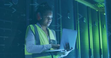 Güvenlik yeleği ve kulaklık takmış sunucu odasında dizüstü bilgisayarla çalışan biri. Teknoloji, siber güvenlik, veri merkezi, ağ, bilişim uzmanı, teknisyeni