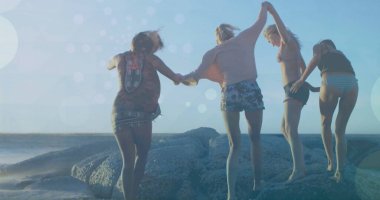 El ele tutuşup kayalara atlamak, arkadaşlar Bokeh imajıyla plaj gününün tadını çıkarmak. Eğlence, macera, açık hava, yaz, mutluluk, doğa