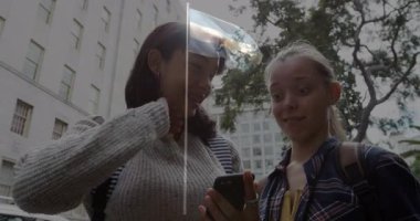 Dışarıda kadınlar birlikte akıllı telefon kullanıyor, gülümsüyor ve animasyon içeriğini izliyorlar. Teknoloji, cep telefonu, iletişim, arkadaşlık, eğlence, eğlence