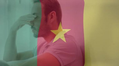 Başı aşağıda oturan, Kamerun bayrağı renkleri ve yıldız animasyonlarıyla örtülü bir adam. Üzüntü, vatanseverlik, umutsuzluk, üst üste, kültürel, ulusal