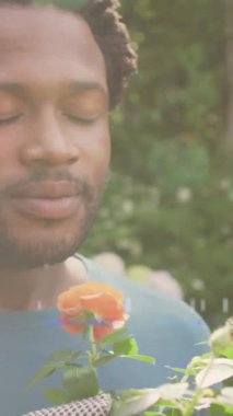 Afro-Amerikan bir adamın bahçedeki çiçekleri koklaması üzerine parlayan ışıkların animasyonu. Bahçe işleri ve halk bahçesi haftası konsepti dijital olarak oluşturulmuş video.