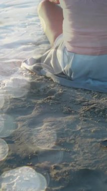 Sahilde yoga yapan ve meditasyon yapan yaşlı beyaz bir kadının üzerinde ışık lekeleri. dünya meditasyon günü ve dijital olarak üretilen video konsepti.