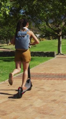 Parkta elektrikli scooter kullanan Afrikalı Amerikalı kadınlara karşı birden fazla yeşil yaprak ikonu var. yeşil çevre kavramı