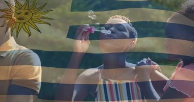 Uruguay bayrak animasyonuyla baloncuklar savuran, güneşli açık hava ortamındaki insanlar. Kutlama, vatanseverlik, ulusal, mutluluk, açık hava, yaz