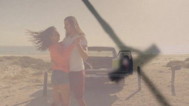 Kumsaldaki kamyonetin yanında kucaklaşan çift, okyanus manzarası ve güneş ışığının tadını çıkarıyorlar. Romantizm, günbatımı, açık hava, seyahat, boş zaman