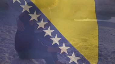 Kumlu plajda, Bosna-Hersek bayrak animasyon örtüsüyle oturan kişi. Kıyı şeridi, vatanseverlik, seyahat, yaz, tatil, huzur