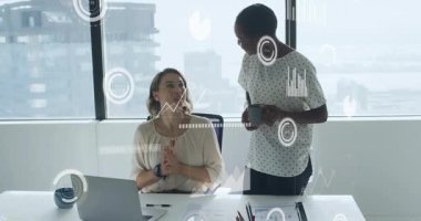 İki kadın çalışma masasında veri işleme animasyon örtüsüyle çalışmayı tartışıyor. İş, takım çalışması, işbirliği, teknoloji, veri analizi, dijital