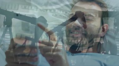 Akıllı telefon kullanarak, arka planda yağ pompası hareketleriyle gülümseyen bir adam. Fosil yakıt, petrol, enerji, çıkarma, dijital, teknoloji