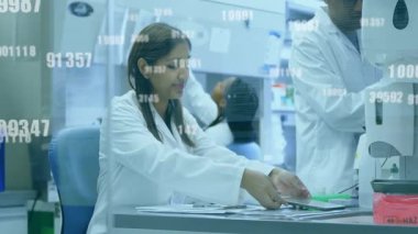 Laboratuvarda laboratuvar önlüklü bilim adamları dijital verileri animasyon örtüsüyle analiz ediyorlar. Araştırma, analiz, yenilik, teknoloji, işbirliği, deney