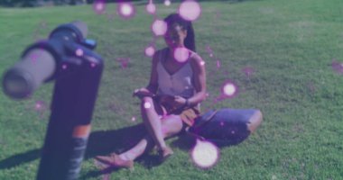 Parkta çim üzerinde oturmuş kitap okuyan bir kadının üzerinde süzülen mor şekiller. Dijital arayüz küresel spor ve performans konsepti dijital olarak oluşturulmuş görüntü.