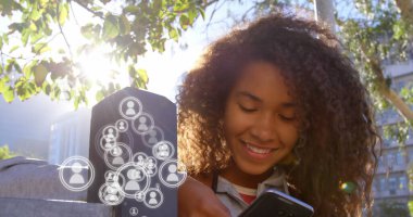 Sosyal medya simgeleriyle akıllı telefon kullanan Afro-Amerikan kadın açık havada gülümsüyor. Teknoloji, sosyal ağ, neşeli, bağlantı, uygulamalar, kablosuz