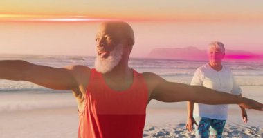 Sahilde yoga yaparken, yaşlı bir çift birlikte gün batımının tadını çıkarıyor. Meditasyon, sağlık, rahatlama, sükunet, okyanus, huzur