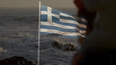 Deniz kenarında çocuk taşıyan, animasyon sahnesinde sallanan Yunan bayrağı taşıyan kişi. Plaj, ebeveynlik, seyahat, aile, kültür, tatil