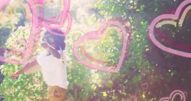 Gözlük takan bir çocuk bahçede pembe kalp animasyonlarıyla neşeyle koşuyor. Çocukluk, mutluluk, açık hava, bahar, oyun, masumiyet.