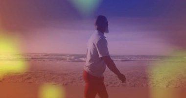 Renkli gökyüzü animasyonu altında, adam sahilde yürüyor, manzaranın tadını çıkarıyor. Günbatımı, seyahat, rahatlama, dinlenme, tatil, huzur