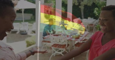 Gana bayrağıyla kucaklaşan iki kişi, açık hava yemek alanının yanında duruyor. Vatanseverlik, kutlama, çeşitlilik, birlik, dostluk, gurur