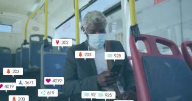 Otobüste maske takan, sosyal medya tebligatları için telefonu kullanan bir adam. Gidiş-dönüş, toplu taşıma, mobil, teknoloji, güvenlik, mesajlaşma