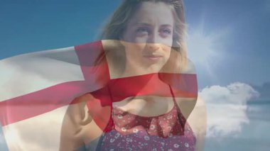 İngiliz bayrağı animasyonunu tutan, mavi gökyüzüne gülümseyen bir kadın. Vatanseverlik, kutlama, ifade, mutluluk, gurur