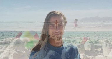 Elinde renkli bir plaj topu, kumsalda yürüyen insanlarla gülümseyen biri. Tatil, mutluluk, eğlence, yaz, açık hava, kıyı şeridi