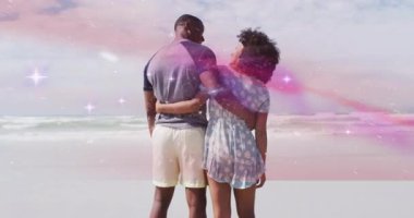 Kumsalda, çift gökkuşağı animasyonu ve parıltılı efektlerle kucaklaşıyor. Romantizm, aşk, kutlama, mutluluk, birliktelik, sihir