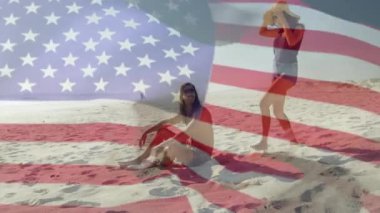 Kumsalda, insanlar güneşli havada Amerikan bayrağı animasyonuyla oynuyorlar. Vatanseverlik, açık hava, kutlama, özgürlük, tatil, eğlence