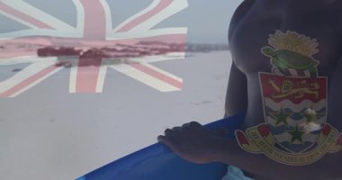 Elinde Cayman Adaları bayrağı olan kaslı bir adam sahilde hareketli bir şekilde dikiliyor. Kaslar, vatanseverlik, okyanus, fitness, yaz, rahatlama