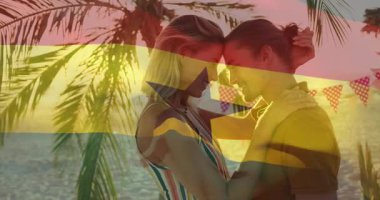Sahilde Gana bayrağı animasyonu ve palmiye ağaçlarıyla kucaklaşan bir çift. Tatil, romantizm, tropik, seyahat, aşk, sahil