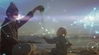 Anne ve bebek kumsalda oynuyor ve ağ bağlantıları ile animasyon örtüşüyor. Aile, bağ, teknoloji, dijital, ebeveynlik, tatil