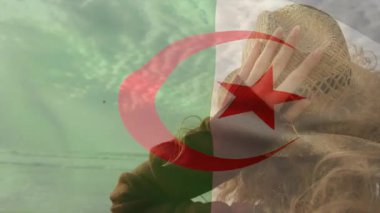 Cezayir bayrağı taşıyan şapkalı, bulutlu arka planda duran biri. Vatanseverlik, ulusal gurur, kimlik, gelenek, kültür, birlik