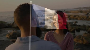 Sahilde gülümseyen bir çift, ön planda Fransız bayrağı animasyonu var. seyahat, romantizm, yaz, tatil, aşk